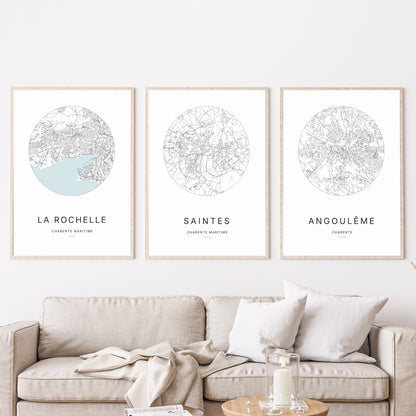 Composition murale de trois affiches minimalistes de villes (Saintes, La Rochelle, Angoulême) encadrées au-dessus d’un canapé dans un salon moderne.