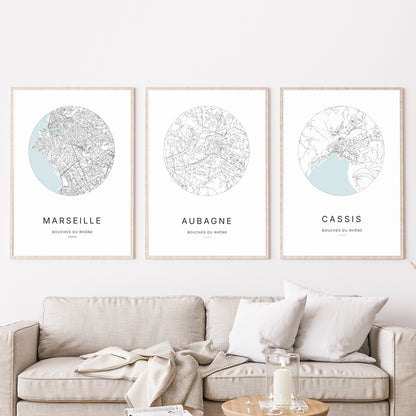 Composition murale de trois affiches minimalistes de villes (Aubagne, Marseille, Cassis) encadrées au-dessus d’un canapé dans un salon moderne.