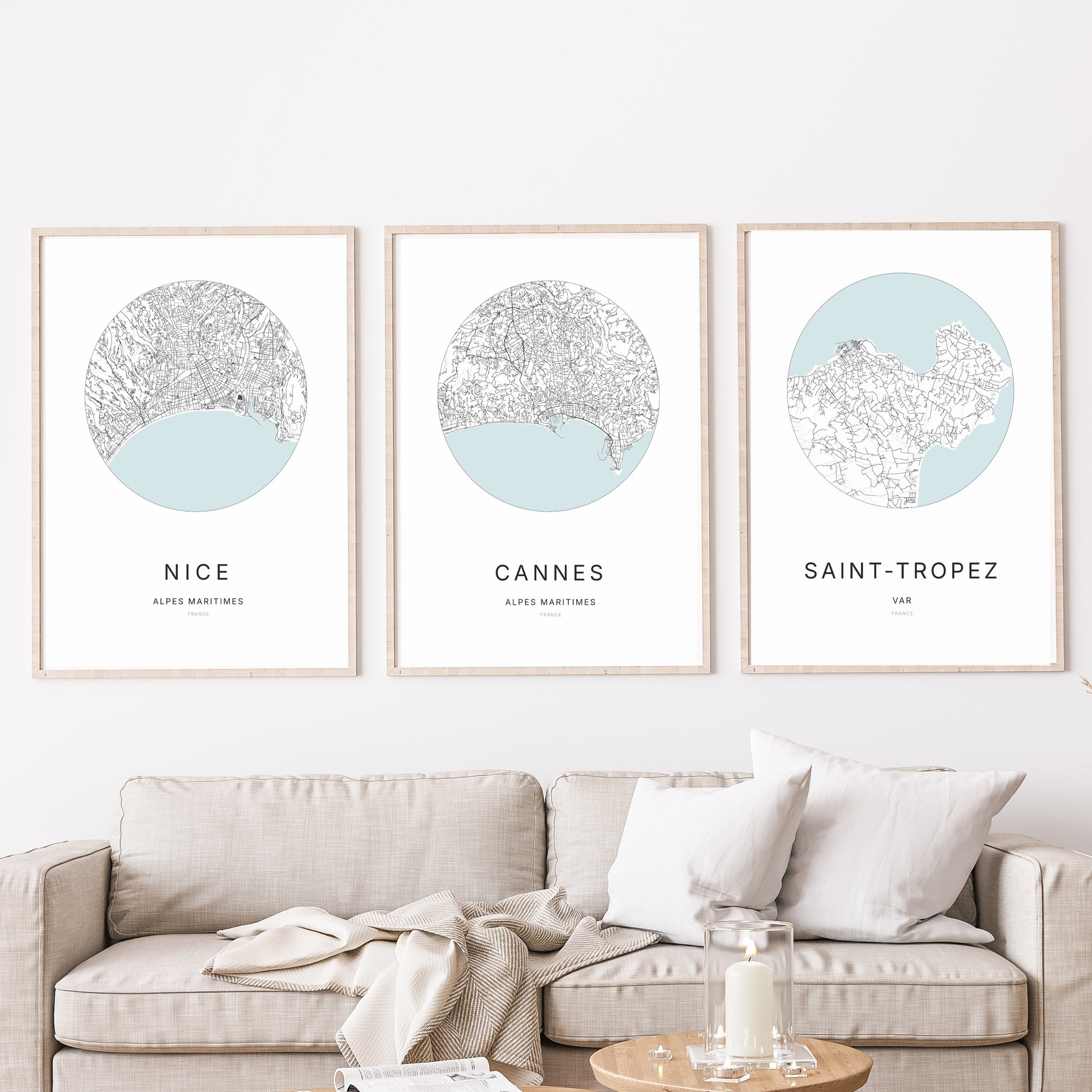 Composition murale de trois affiches minimalistes de villes (Cannes, Nice, Saint tropez) encadrées au-dessus d’un canapé dans un salon moderne