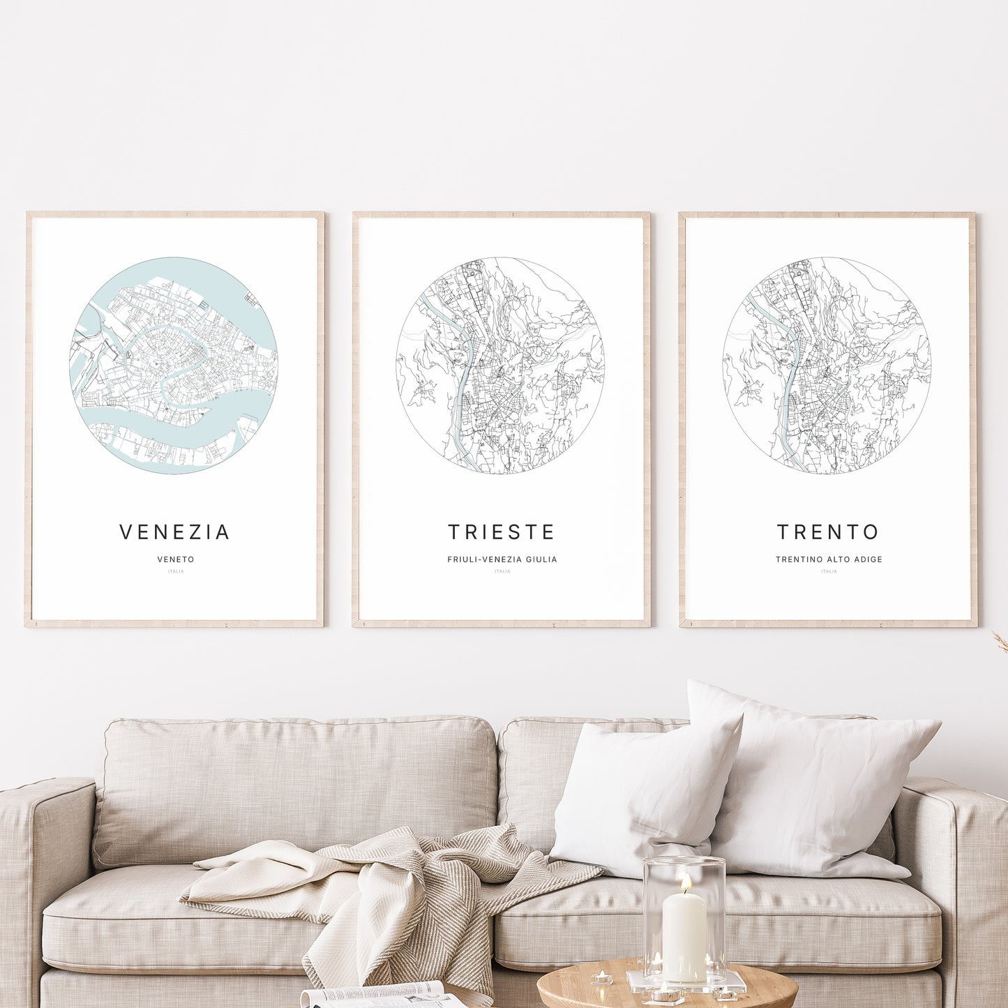 Composition murale de trois affiches minimalistes de villes (Trieste, Venezia, Trento) encadrées au-dessus d’un canapé dans un salon moderne.