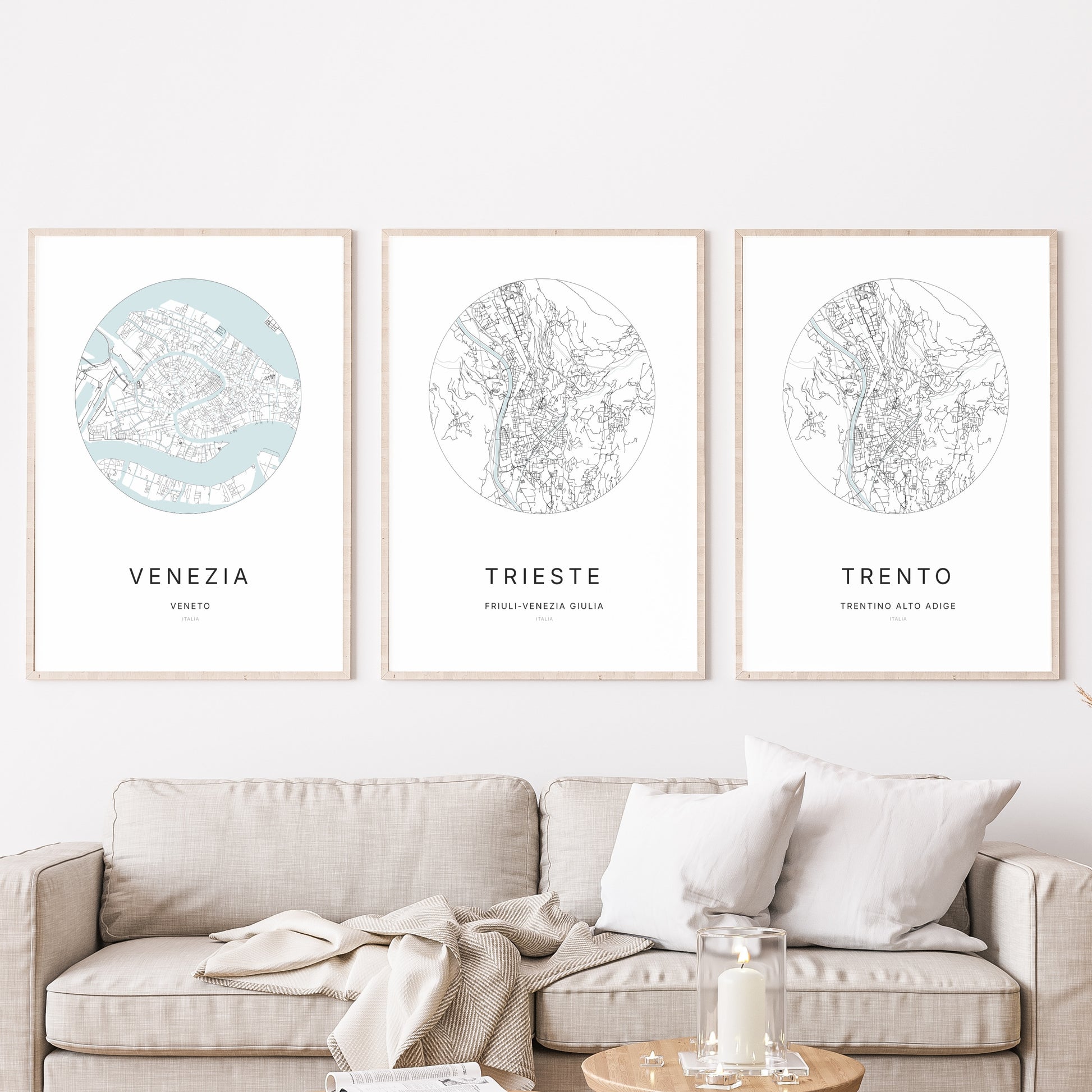Composition murale de trois affiches minimalistes de villes (Trieste, Venezia, Trento) encadrées au-dessus d’un canapé dans un salon moderne.