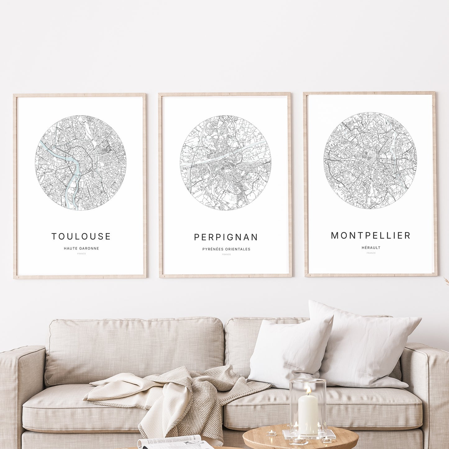 Composition murale de trois affiches minimalistes de villes (Perpignan, Montpellier, Toulouse) encadrées au-dessus d’un canapé dans un salon moderne