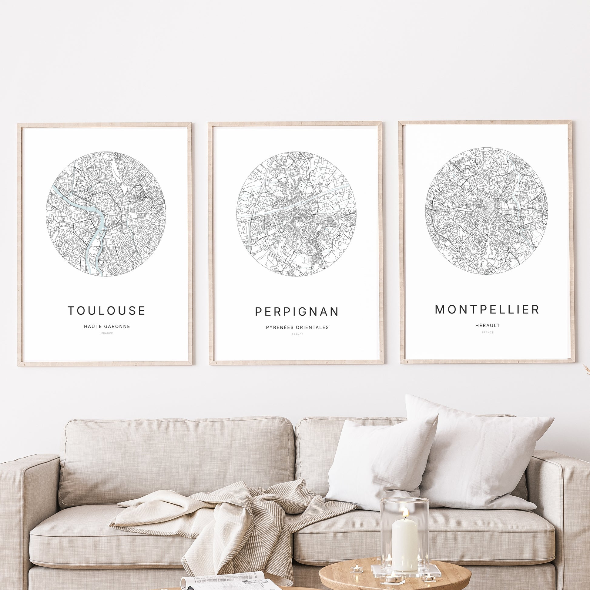 Composition murale de trois affiches minimalistes de villes (Perpignan, Montpellier, Toulouse) encadrées au-dessus d’un canapé dans un salon moderne