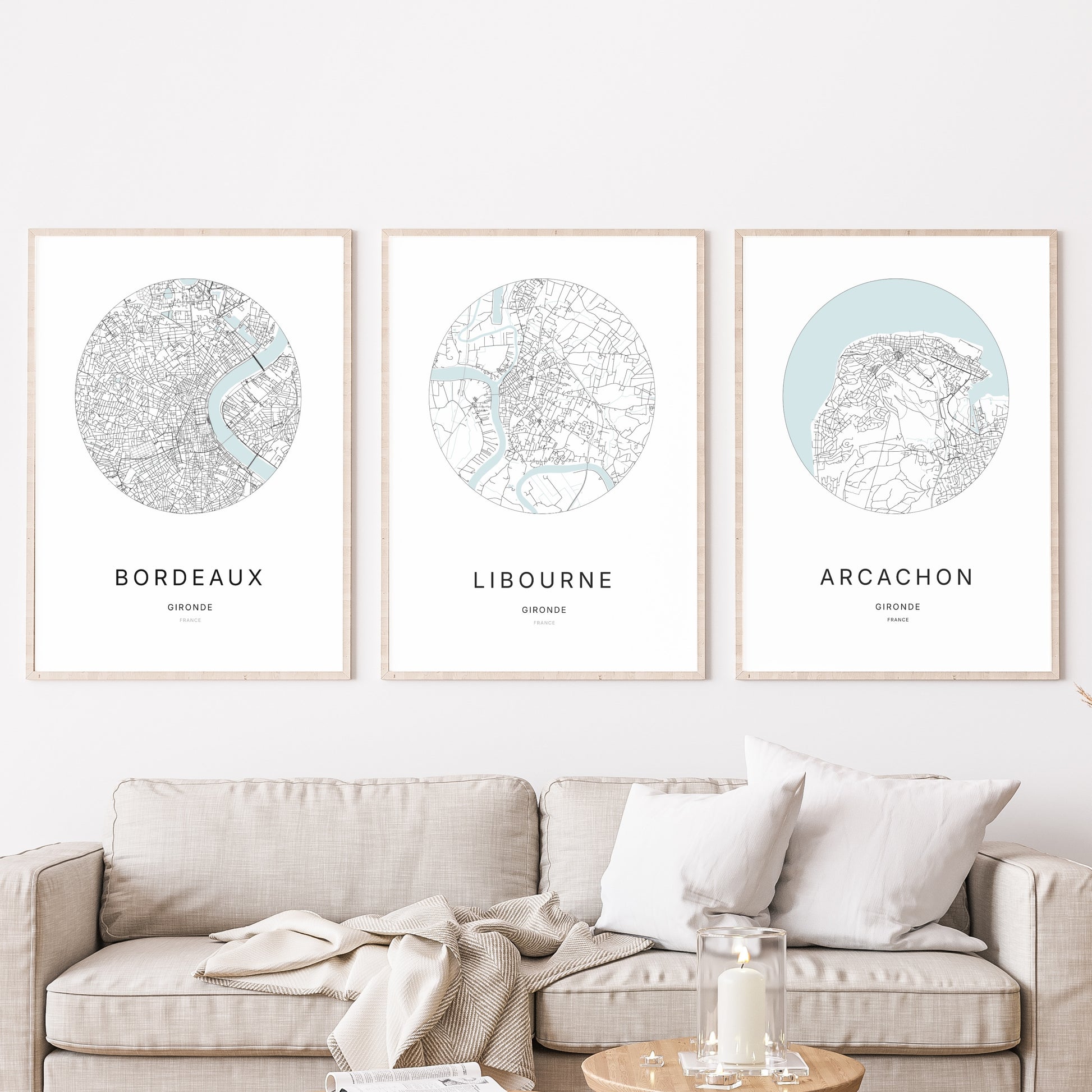 Composition murale de trois affiches minimalistes de villes (Libourne, Bordeaux, Arcachon) encadrées au-dessus d’un canapé dans un salon moderne.