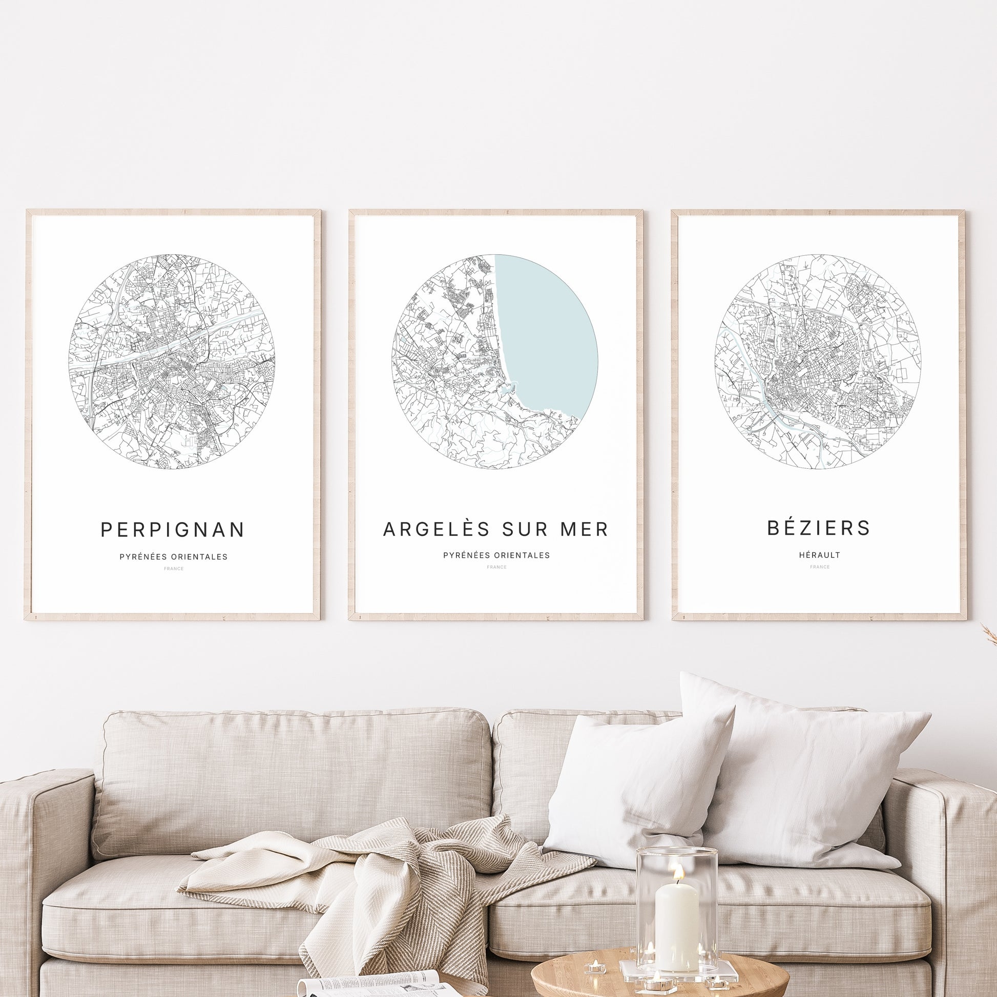 Composition murale de trois affiches minimalistes de villes (Argelès-sur-Mer, Perpignan, Béziers) encadrées au-dessus d’un canapé dans un salon moderne.