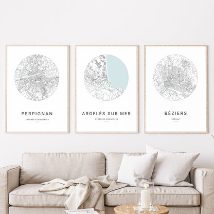 Composition murale de trois affiches minimalistes de villes (Argelès-sur-Mer, Perpignan, Béziers) encadrées au-dessus d’un canapé dans un salon moderne.