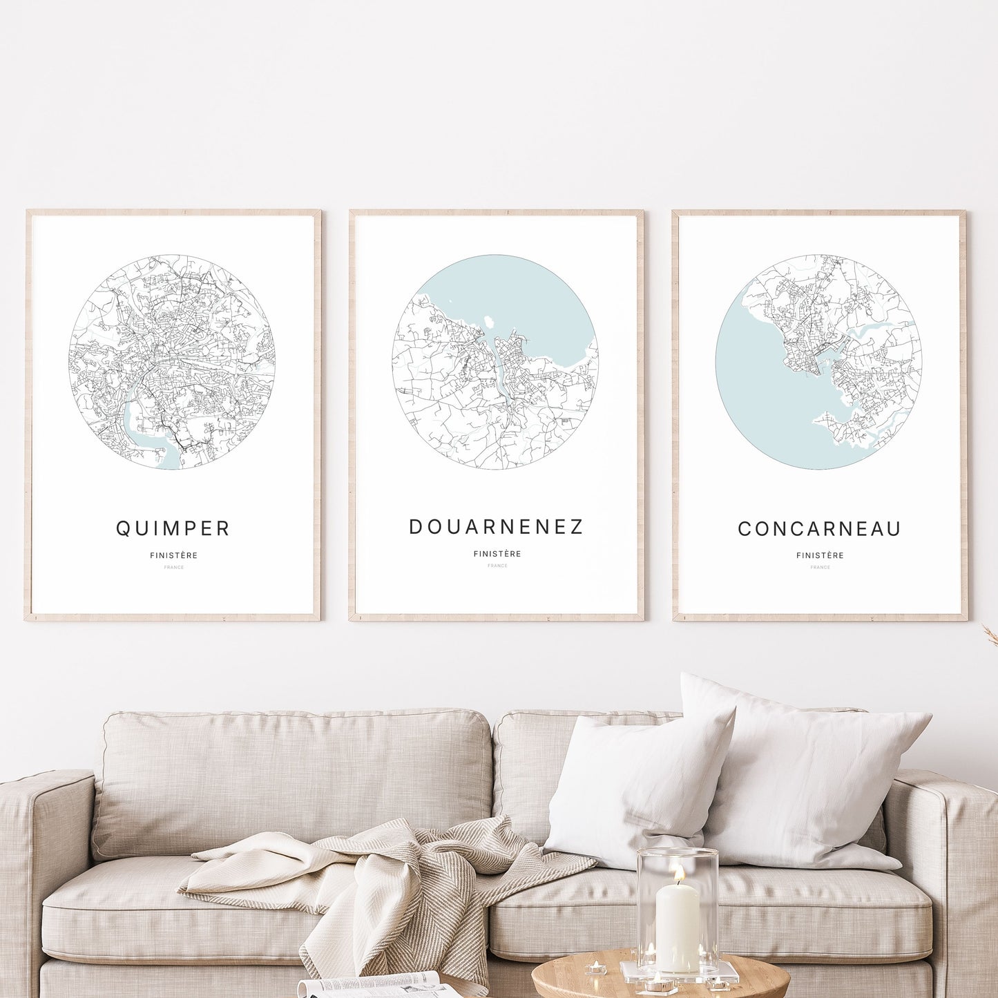 Composition murale de trois affiches minimalistes de villes (Douarnenez, Quimper, Concarneau) encadrées au-dessus d’un canapé dans un salon moderne.