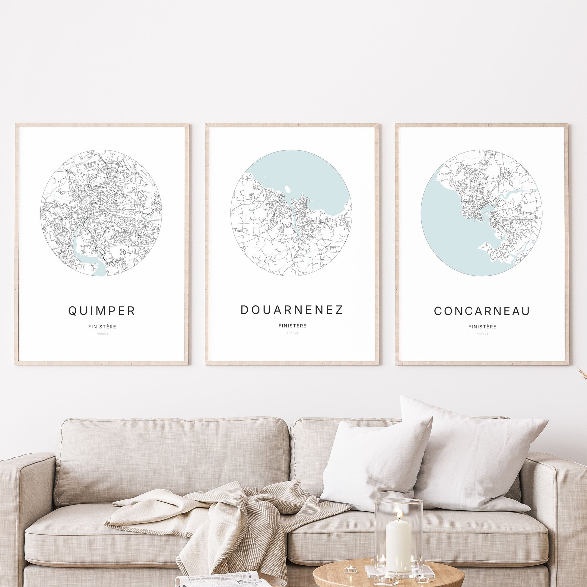 Composition murale de trois affiches minimalistes de villes (Douarnenez, Quimper, Concarneau) encadrées au-dessus d’un canapé dans un salon moderne.