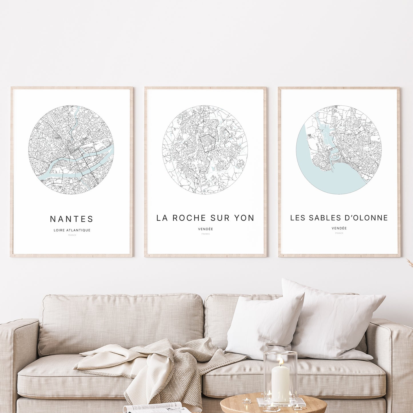 Composition murale de trois affiches minimalistes de villes (La Roche-sur-Yon, Les Sables-d’Olonne, Nantes) encadrées au-dessus d’un canapé dans un salon moderne.