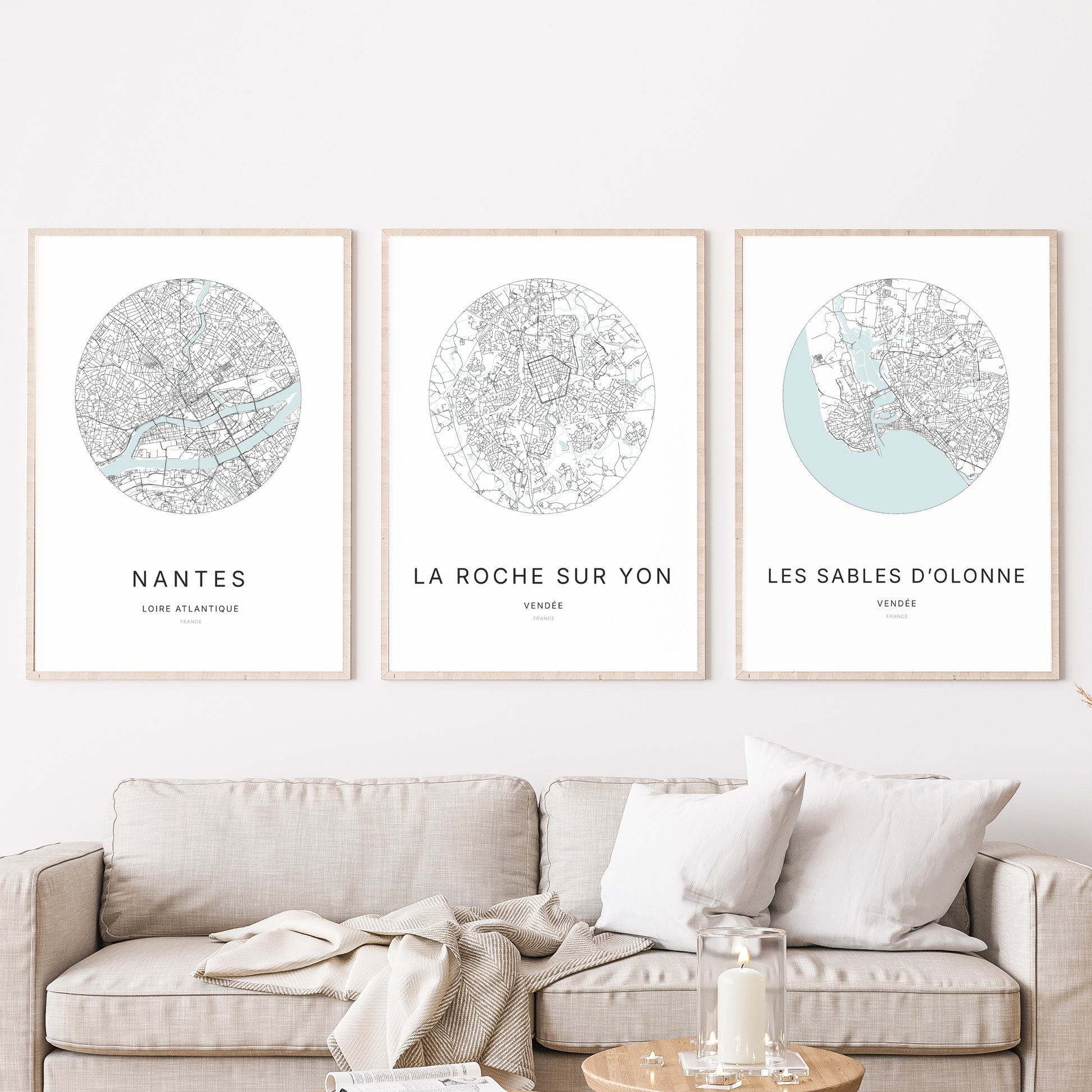 Composition murale de trois affiches minimalistes de villes (La Roche-sur-Yon, Les Sables-d’Olonne, Nantes) encadrées au-dessus d’un canapé dans un salon moderne.