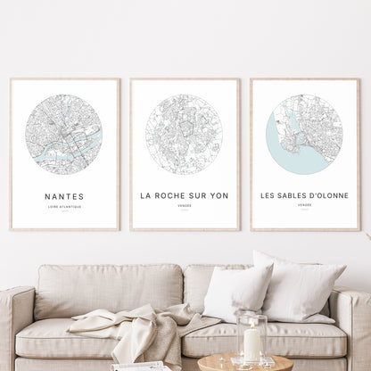 Composition murale de trois affiches minimalistes de villes (La Roche-sur-Yon, Les Sables-d’Olonne, Nantes) encadrées au-dessus d’un canapé dans un salon moderne.