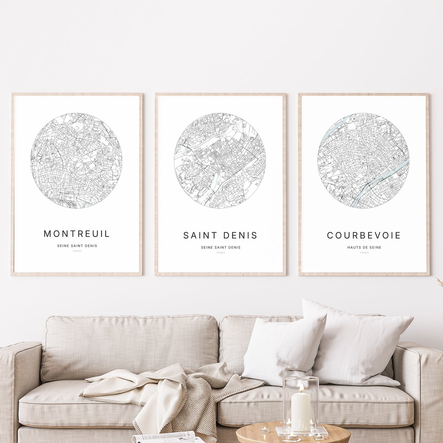 Composition murale de trois affiches minimalistes de villes (Saint-Denis, Montreuil, Courbevoie) encadrées au-dessus d’un canapé dans un salon moderne.