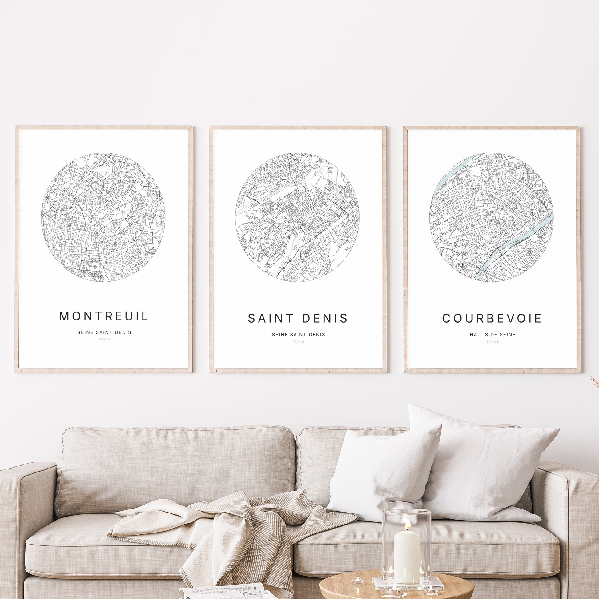 Composition murale de trois affiches minimalistes de villes (Saint-Denis, Montreuil, Courbevoie) encadrées au-dessus d’un canapé dans un salon moderne.