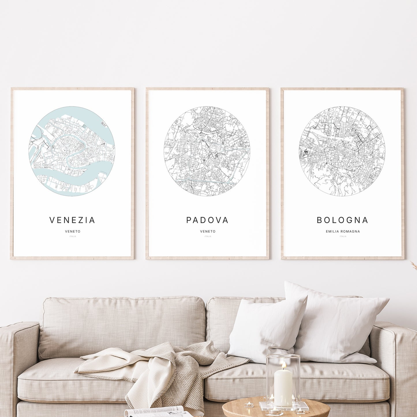 Composition murale de trois affiches minimalistes de villes (Padova, Venezia, Bologna) encadrées au-dessus d’un canapé dans un salon moderne.