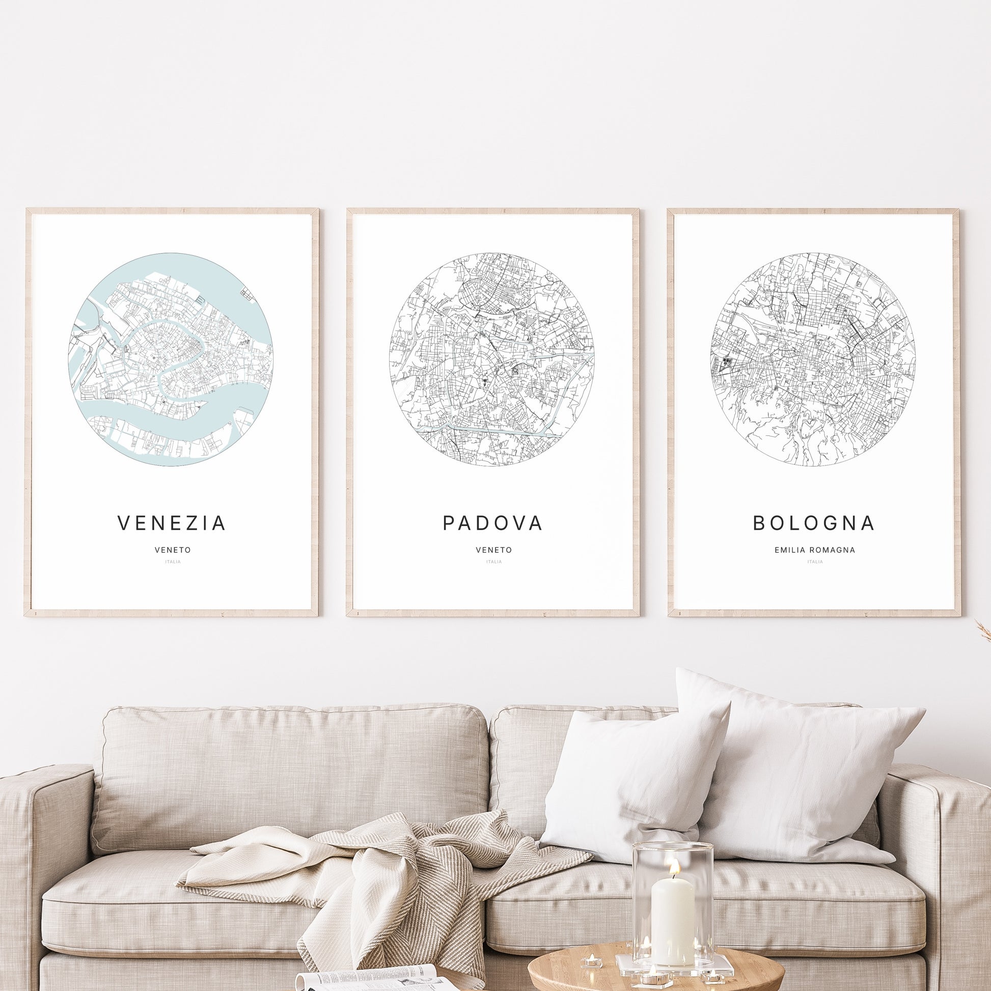 Composition murale de trois affiches minimalistes de villes (Padova, Venezia, Bologna) encadrées au-dessus d’un canapé dans un salon moderne.