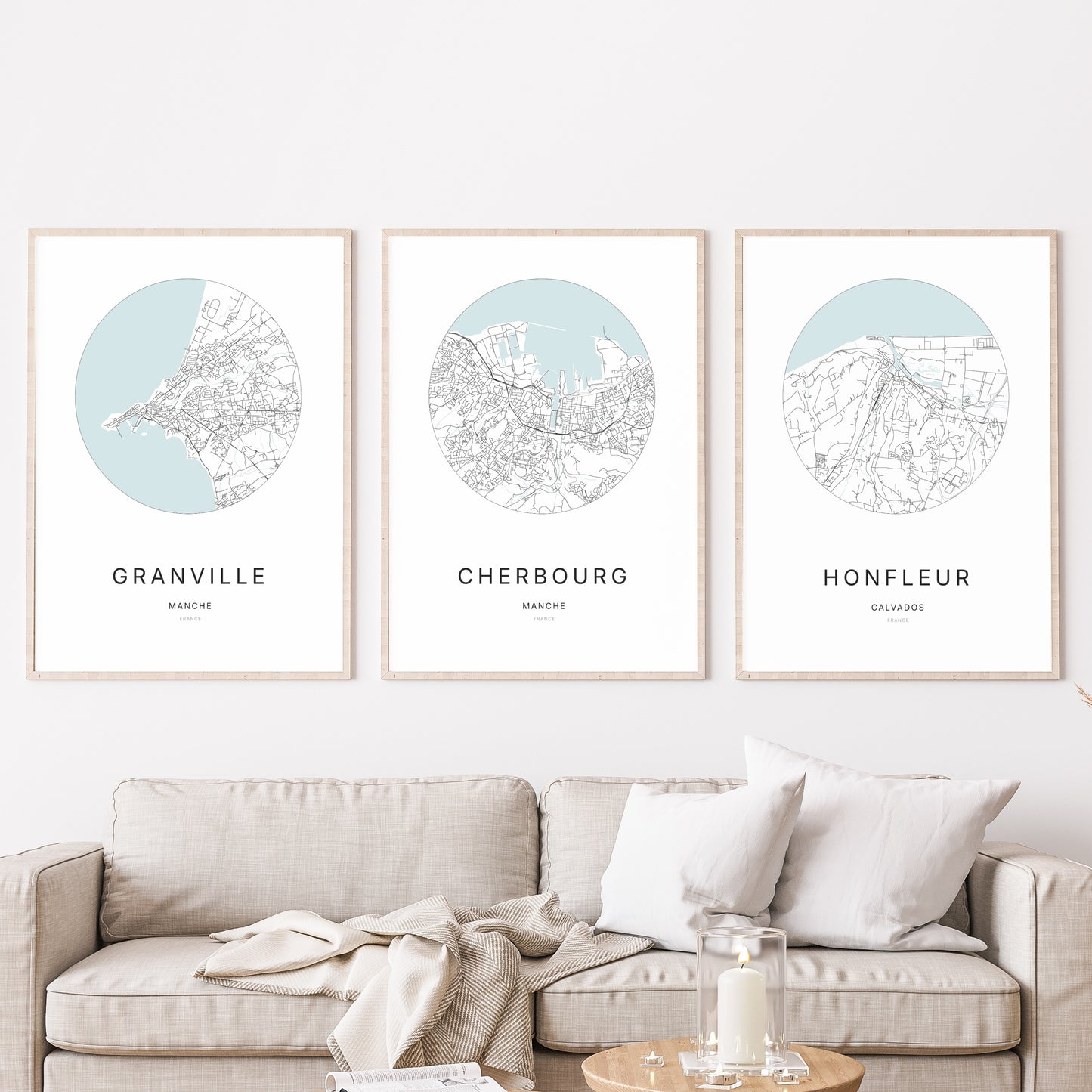 Composition murale de trois affiches minimalistes de villes (Cherbourg, Granville, Honfleur) encadrées au-dessus d’un canapé dans un salon moderne.