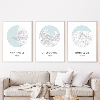 Composition murale de trois affiches minimalistes de villes (Cherbourg, Granville, Honfleur) encadrées au-dessus d’un canapé dans un salon moderne.