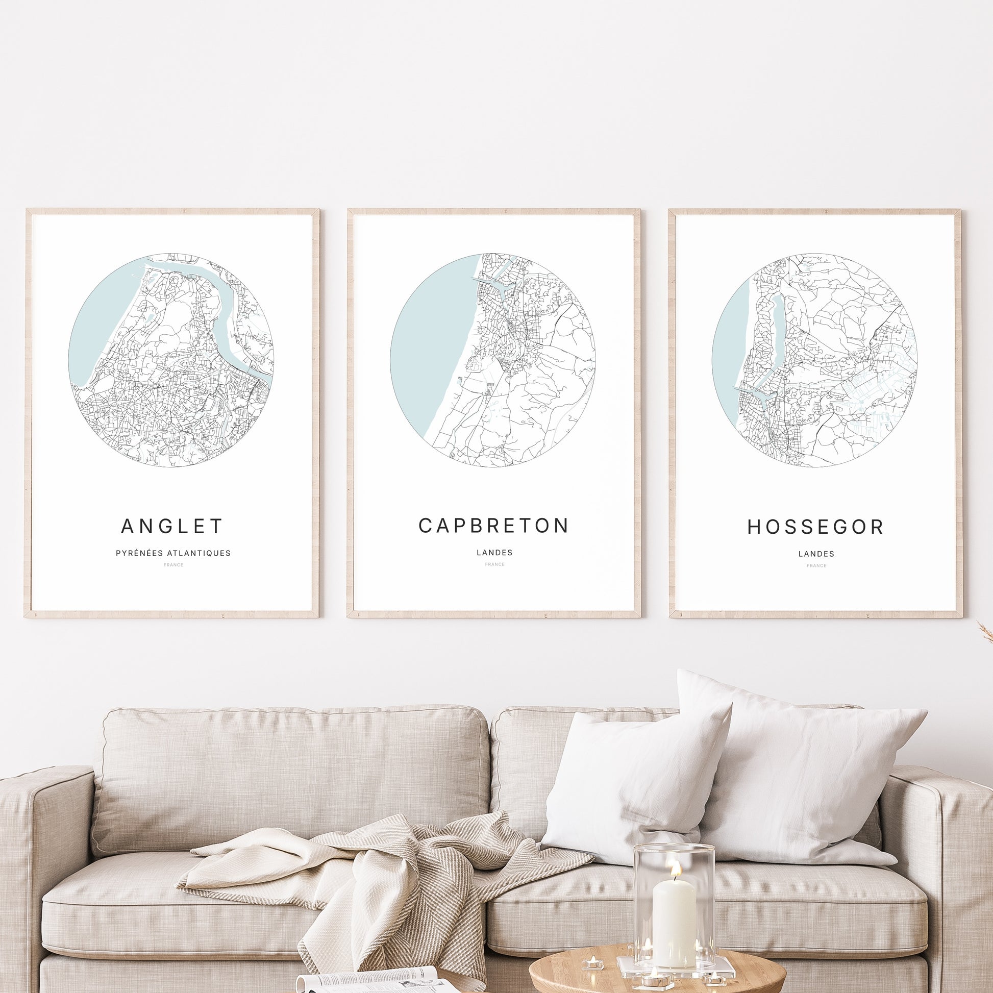 Composition murale de trois affiches minimalistes de villes (Capbreton, Anglet, Hossegor) encadrées au-dessus d’un canapé dans un salon moderne.