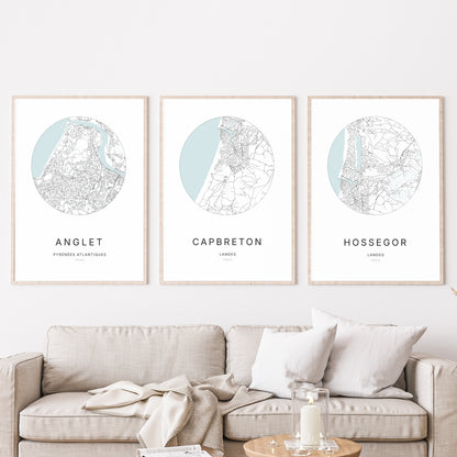 Composition murale de trois affiches minimalistes de villes (Capbreton, Anglet, Hossegor) encadrées au-dessus d’un canapé dans un salon moderne.