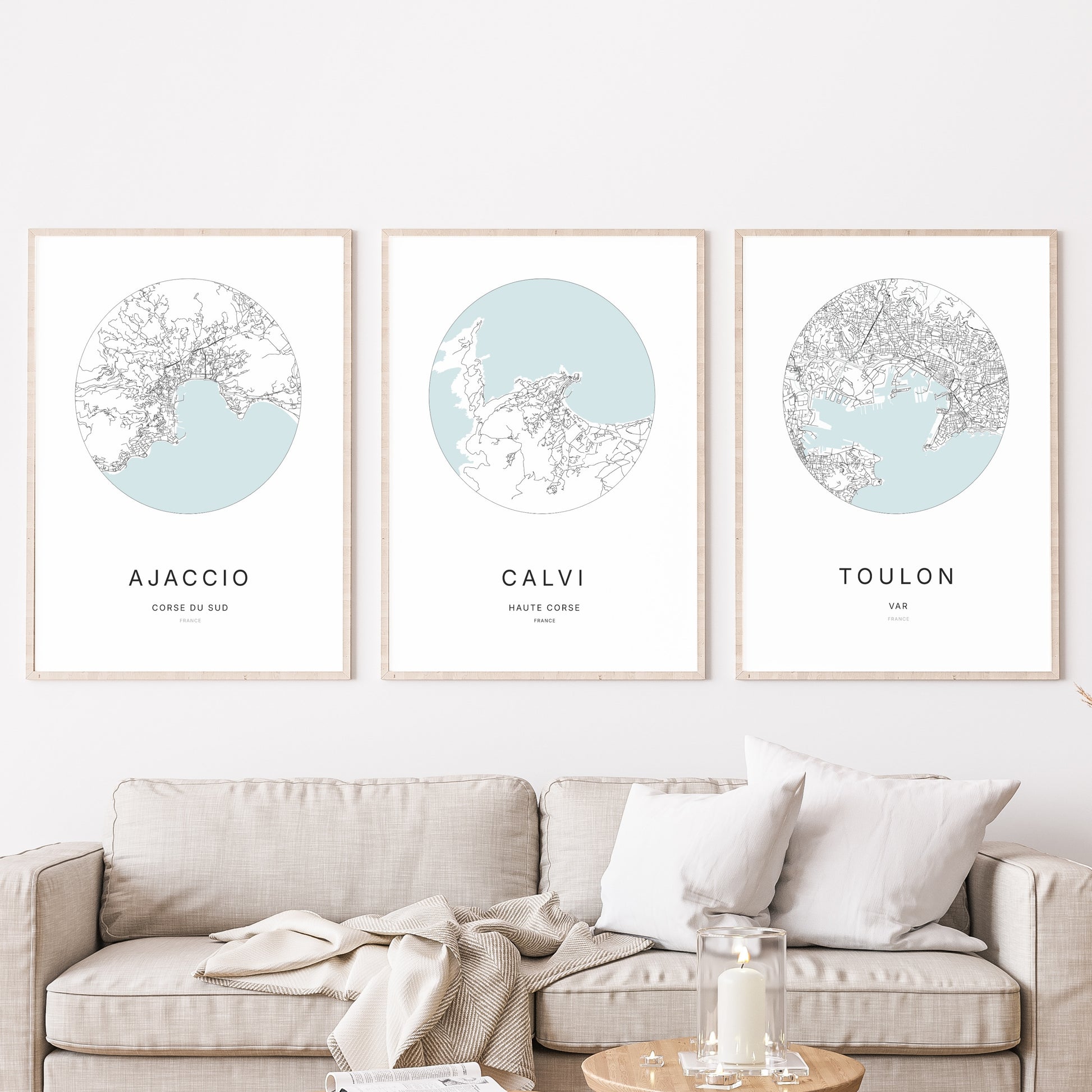 Composition murale de trois affiches minimalistes de villes (Calvi, Ajaccio, Toulon) encadrées au-dessus d’un canapé dans un salon moderne