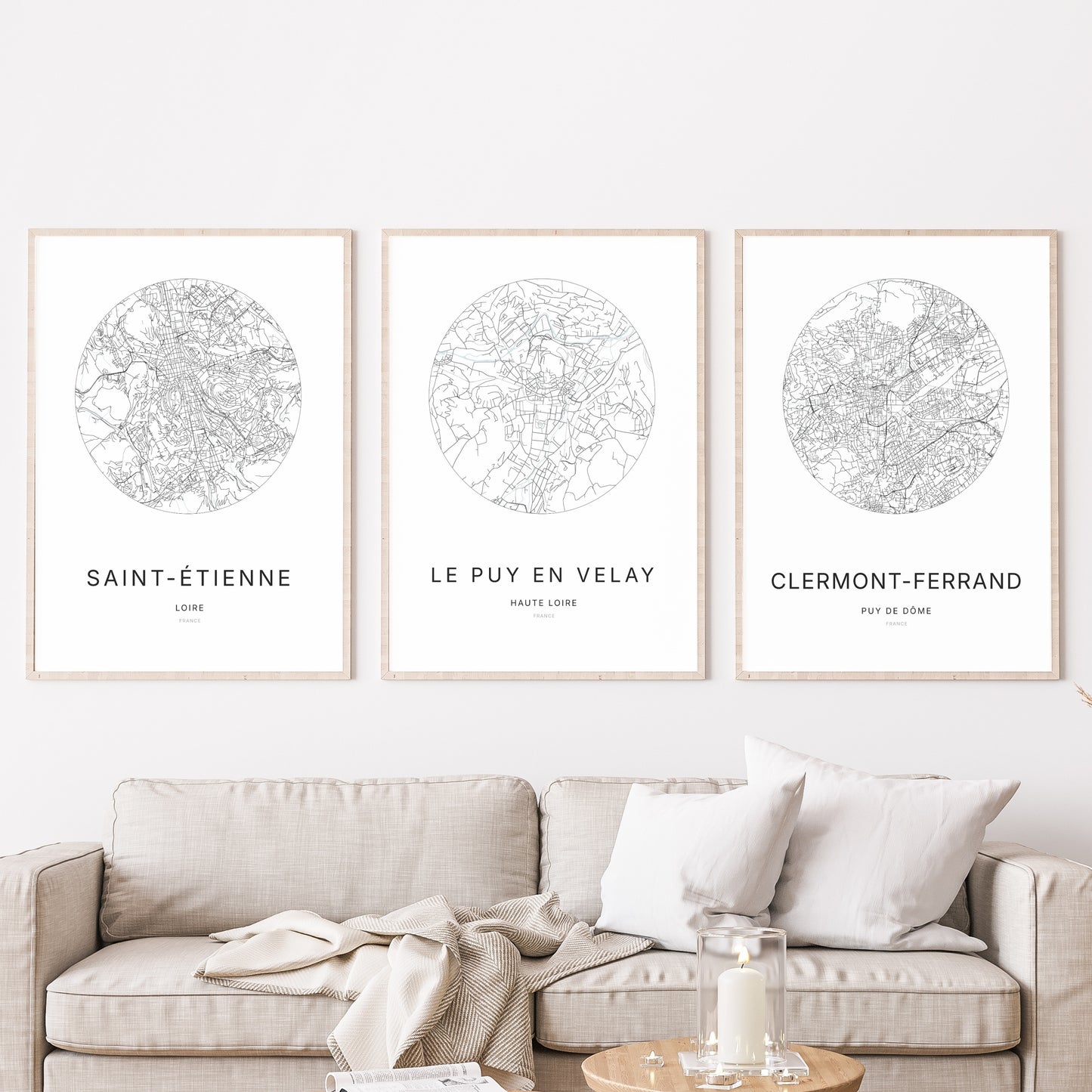 Composition murale de trois affiches minimalistes de villes (Le Puy-en-Velay, Saint-Étienne, Clermont-Ferrand) encadrées au-dessus d’un canapé dans un salon moderne.