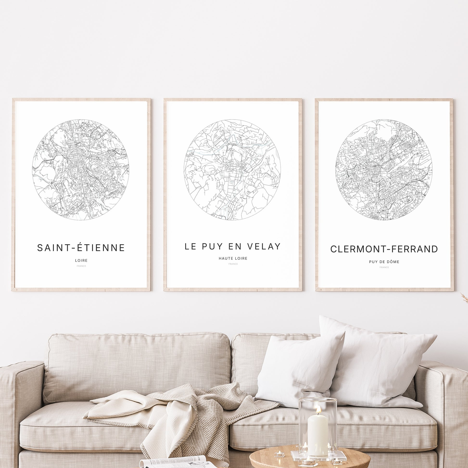 Composition murale de trois affiches minimalistes de villes (Le Puy-en-Velay, Saint-Étienne, Clermont-Ferrand) encadrées au-dessus d’un canapé dans un salon moderne.