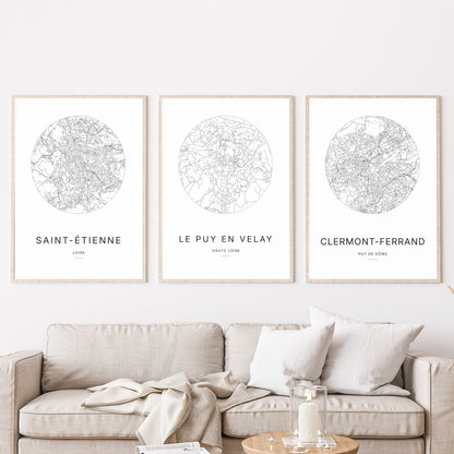 Composition murale de trois affiches minimalistes de villes (Le Puy-en-Velay, Saint-Étienne, Clermont-Ferrand) encadrées au-dessus d’un canapé dans un salon moderne.