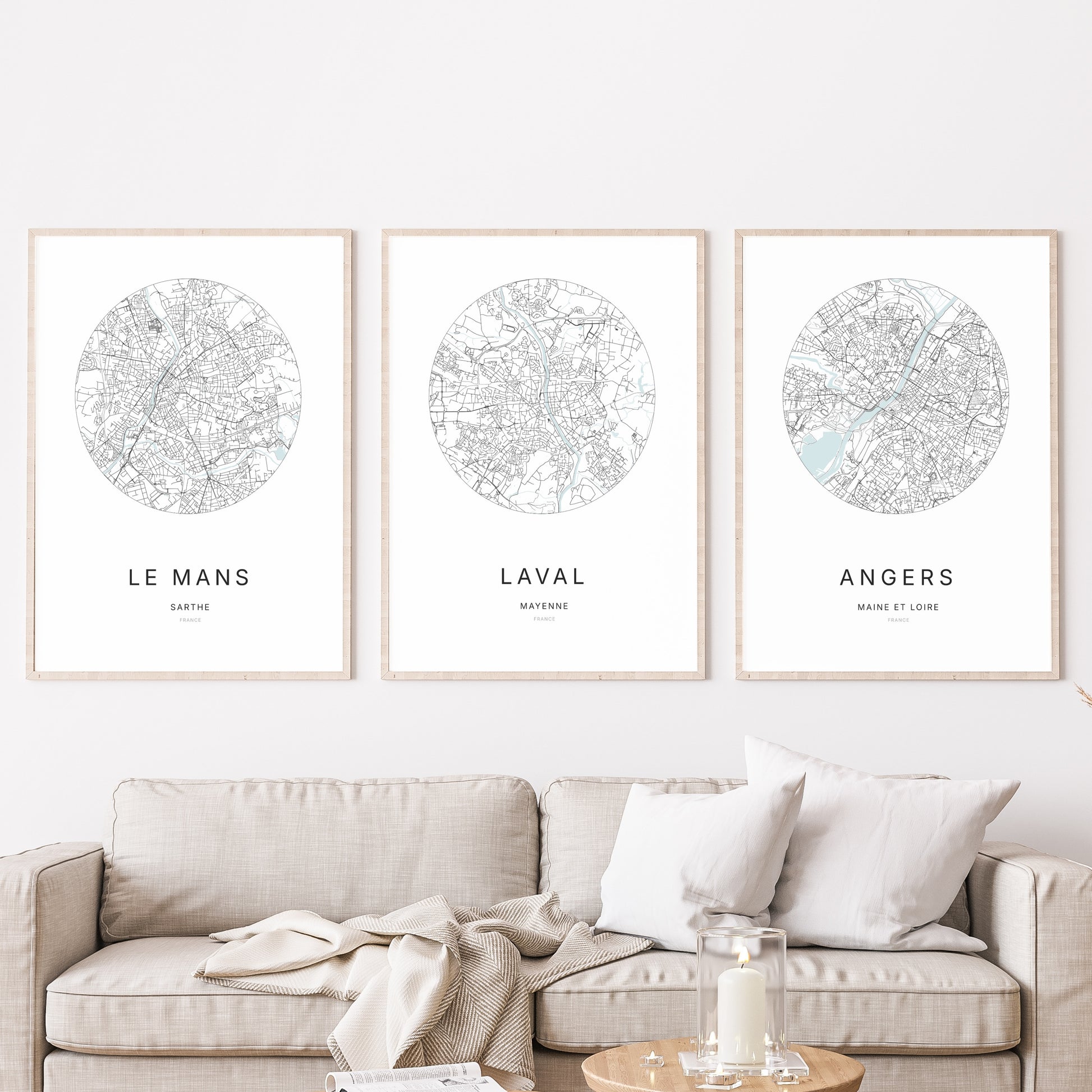 Composition murale de trois affiches minimalistes de villes (Laval, Le Mans, Angers) encadrées au-dessus d’un canapé dans un salon moderne.