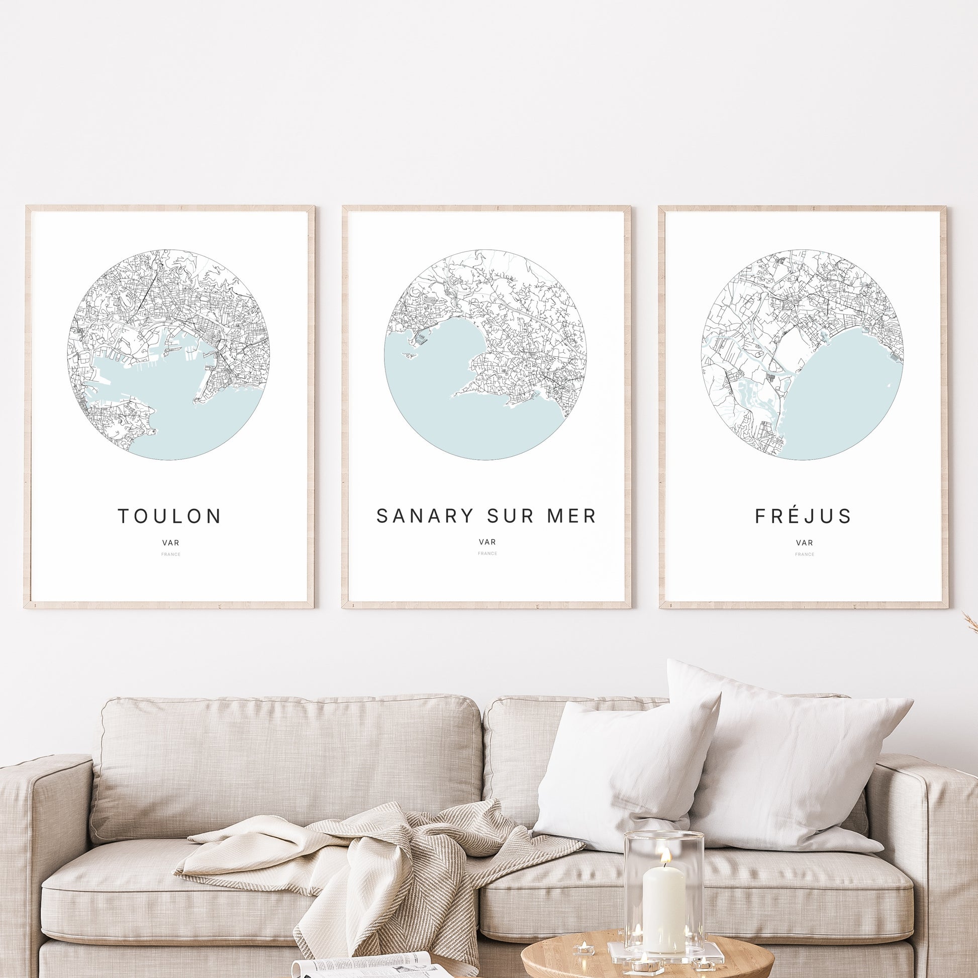 Composition murale de trois affiches minimalistes de villes (Sanary-sur-Mer, Toulon, Fréjus) encadrées au-dessus d’un canapé dans un salon moderne