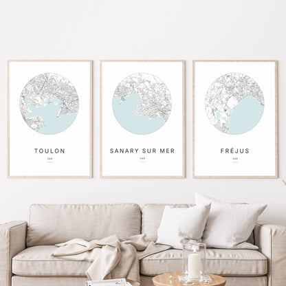 Composition murale de trois affiches minimalistes de villes (Sanary-sur-Mer, Toulon, Fréjus) encadrées au-dessus d’un canapé dans un salon moderne