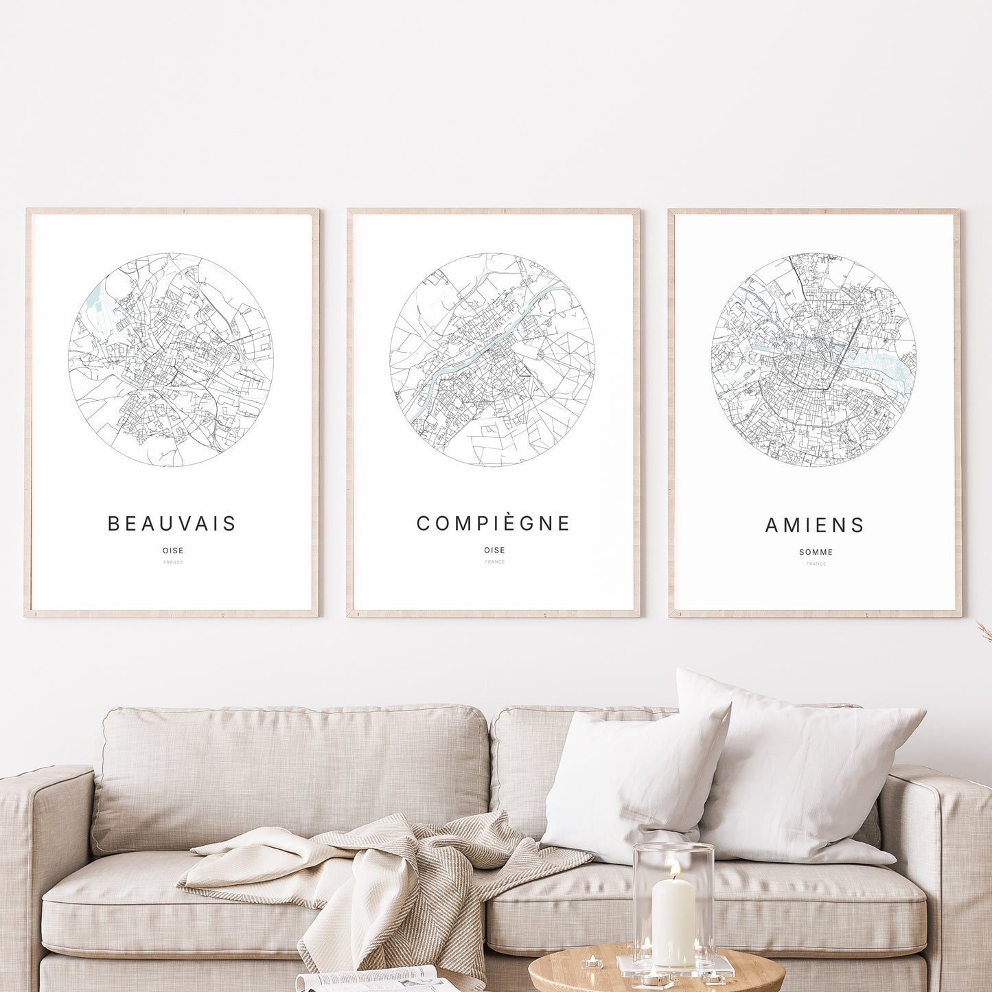 Composition murale de trois affiches minimalistes de villes (Compiègne, Beauvais, Amiens) encadrées au-dessus d’un canapé dans un salon moderne.