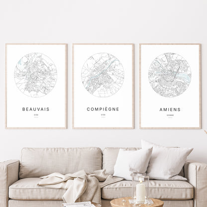 Composition murale de trois affiches minimalistes de villes (Compiègne, Beauvais, Amiens) encadrées au-dessus d’un canapé dans un salon moderne.