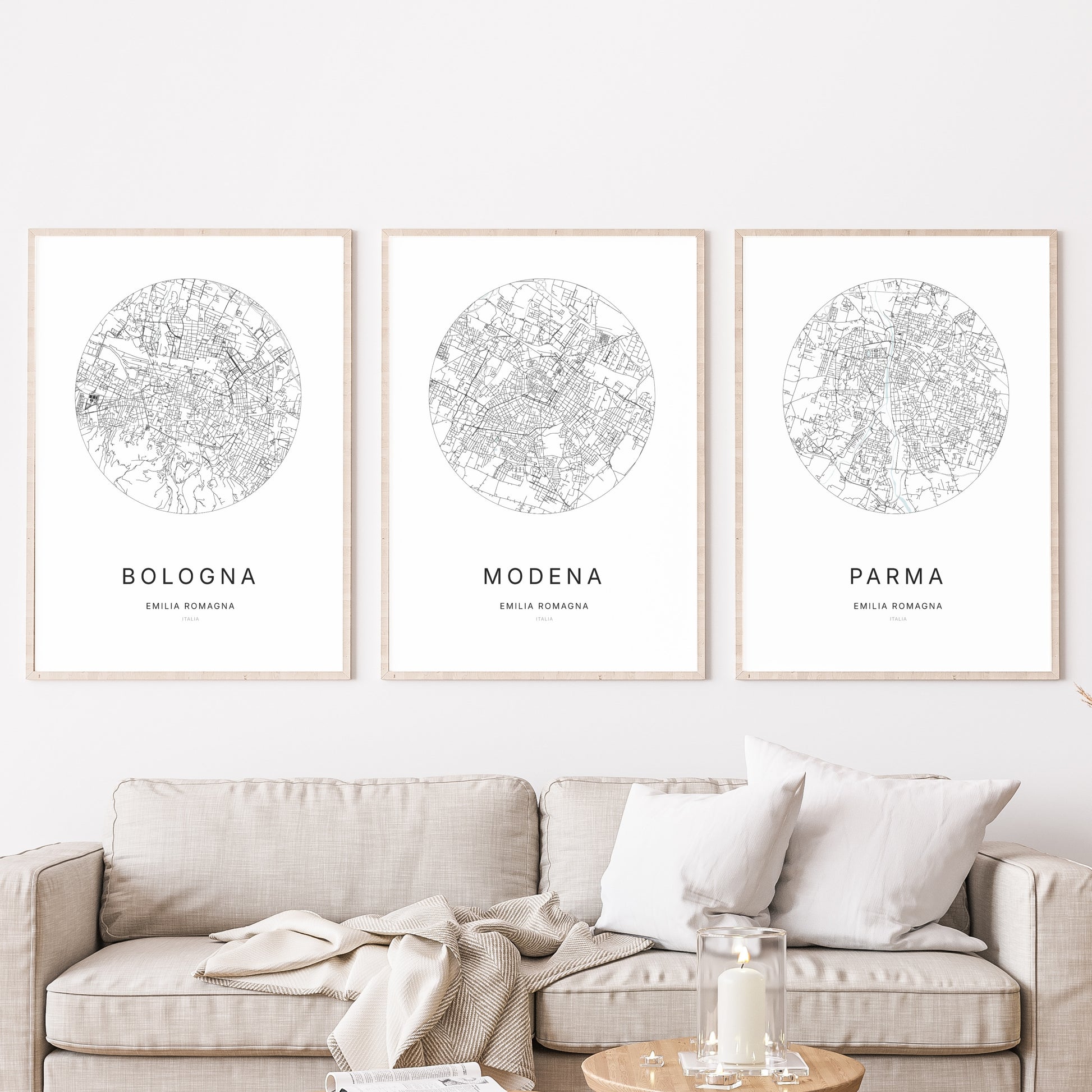 Composition murale de trois affiches minimalistes de villes (Modena, Bologna, Parma) encadrées au-dessus d’un canapé dans un salon moderne.
