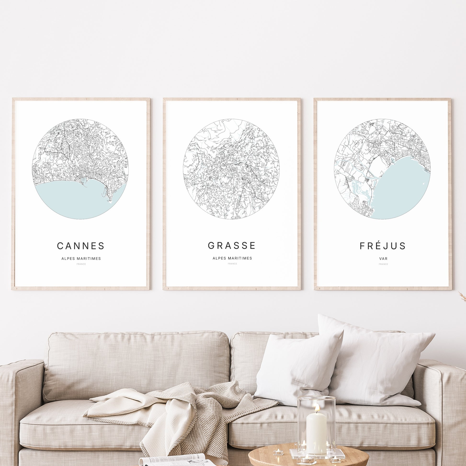 Composition murale de trois affiches minimalistes de villes (Grasse, Cannes, Fréjus) encadrées au-dessus d’un canapé dans un salon moderne.