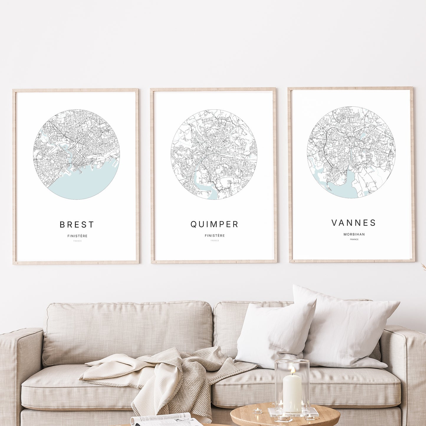 Composition murale de trois affiches minimalistes de villes (Quimper, Vannes, Brest) encadrées au-dessus d’un canapé dans un salon moderne
