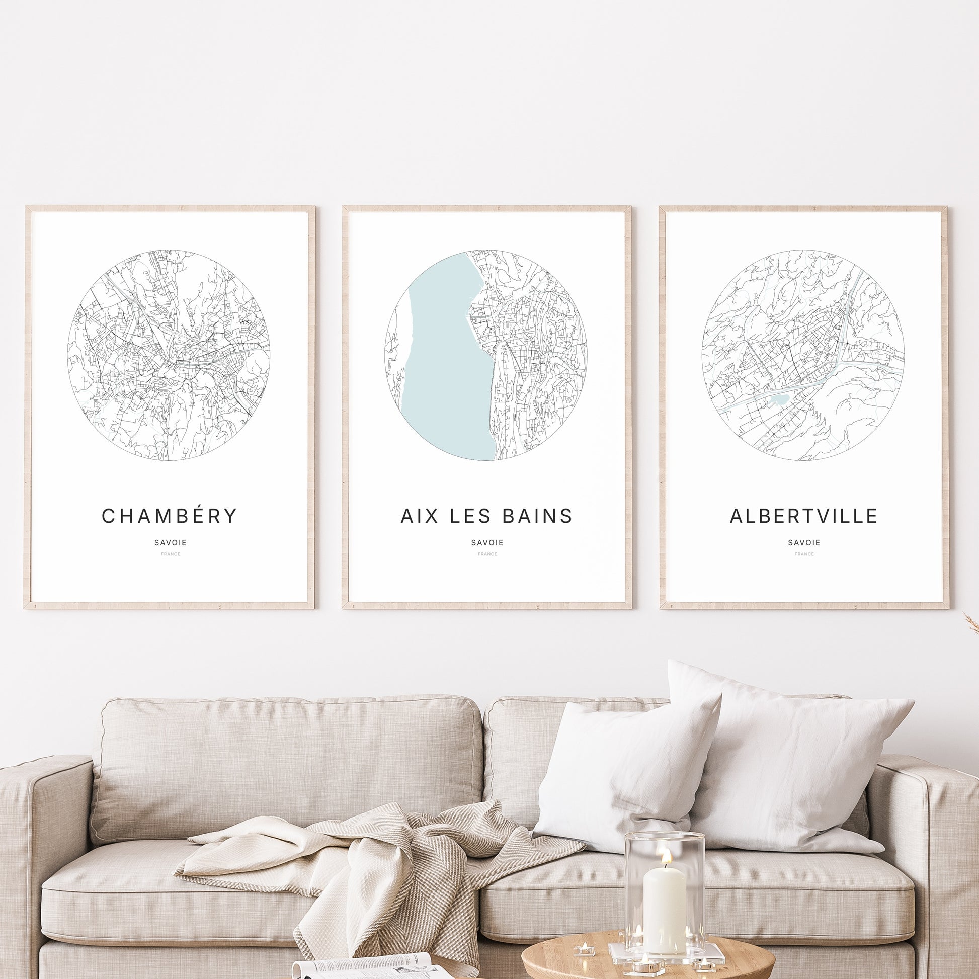 Composition murale de trois affiches minimalistes de villes (Aix-les-Bains, Chambéry, Albertville) encadrées au-dessus d’un canapé dans un salon moderne.