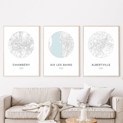 Composition murale de trois affiches minimalistes de villes (Aix-les-Bains, Chambéry, Albertville) encadrées au-dessus d’un canapé dans un salon moderne.