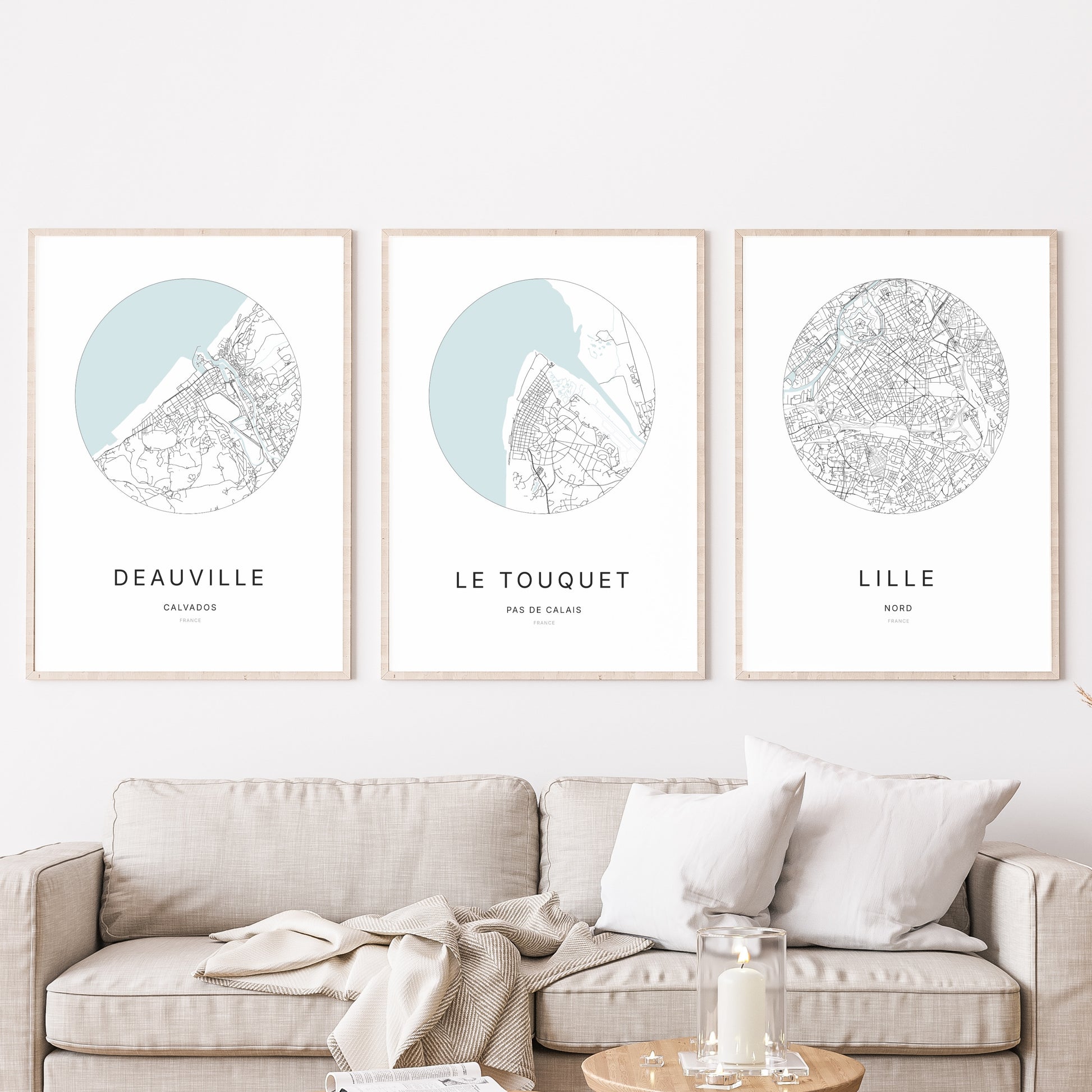 Composition murale de trois affiches minimalistes de villes (Le Touquet, Deauville, Lille) encadrées au-dessus d’un canapé dans un salon moderne.
