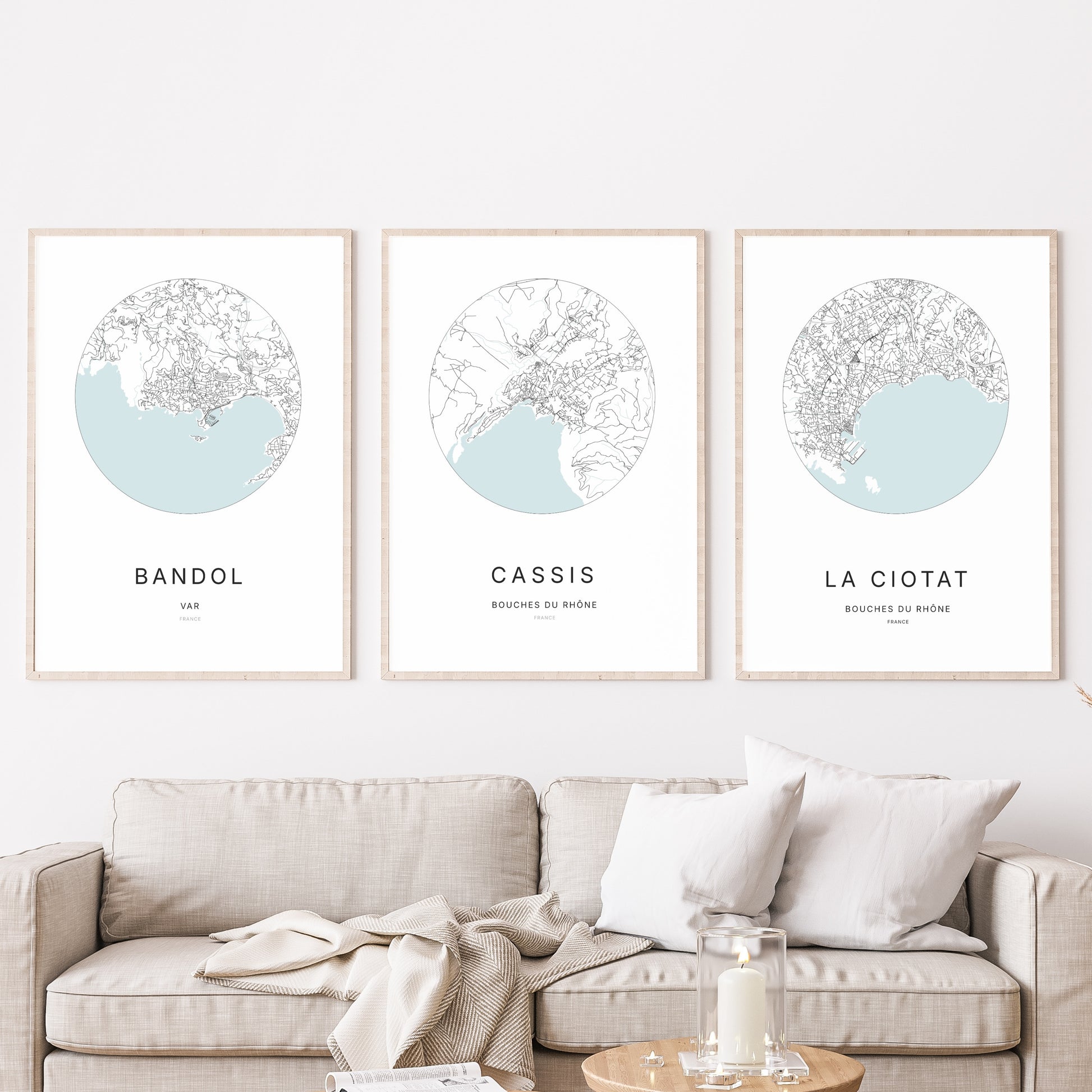 Composition murale de trois affiches minimalistes de villes (Cassis, Bandol, La Ciotat) encadrées au-dessus d’un canapé dans un salon moderne.