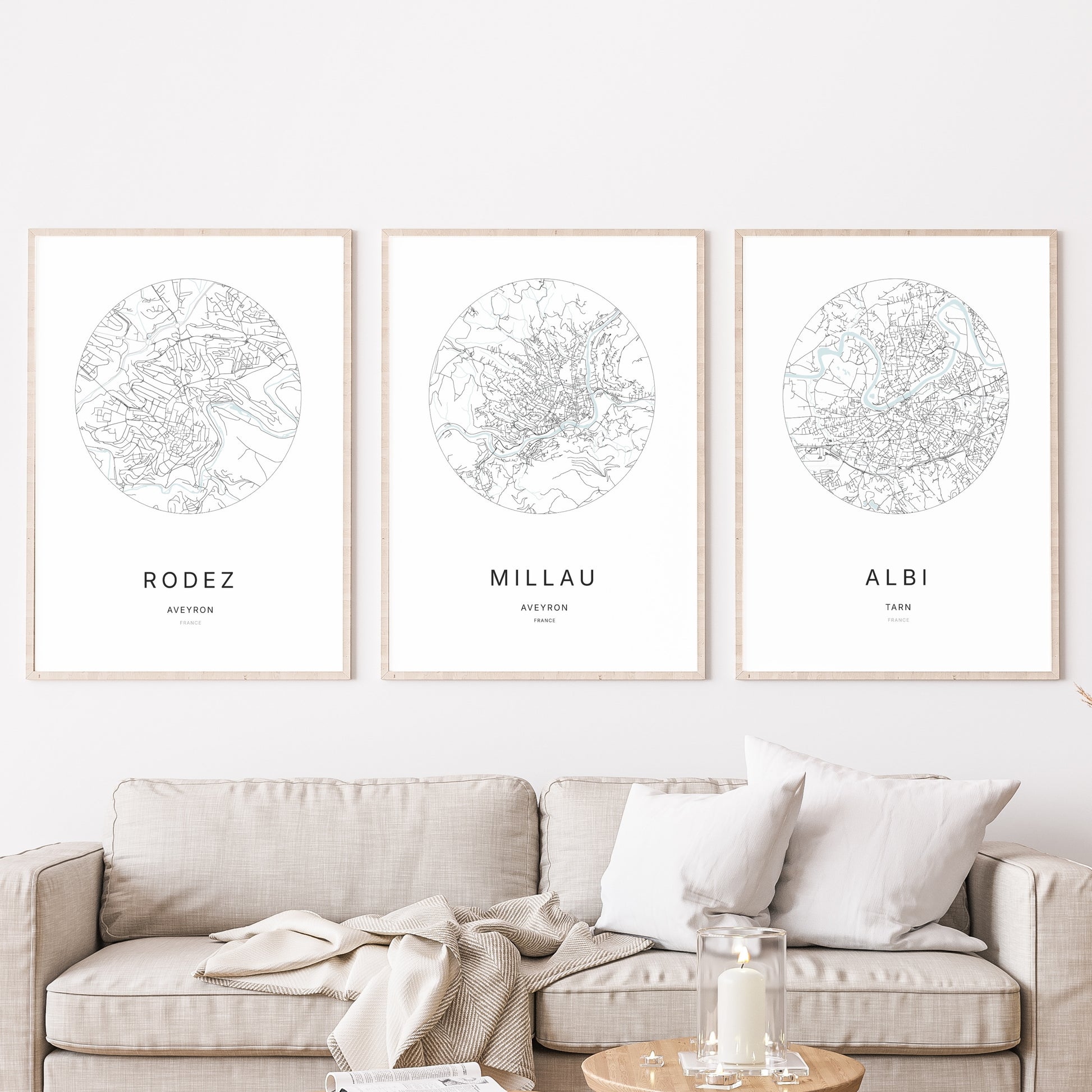 Composition murale de trois affiches minimalistes de villes (Millau, Rodez, Albi) encadrées au-dessus d’un canapé dans un salon moderne.