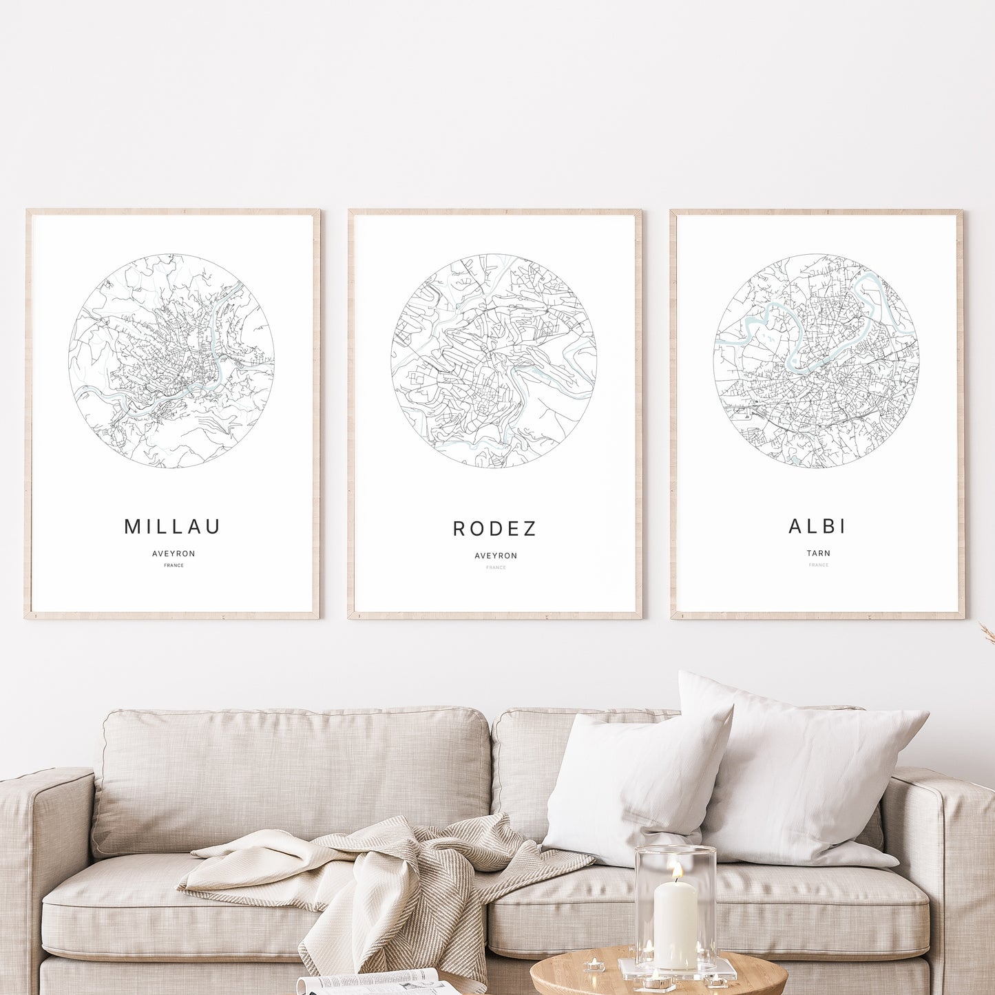 Composition murale de trois affiches minimalistes de villes (Rodez, Millau, Albi) encadrées au-dessus d’un canapé dans un salon moderne.