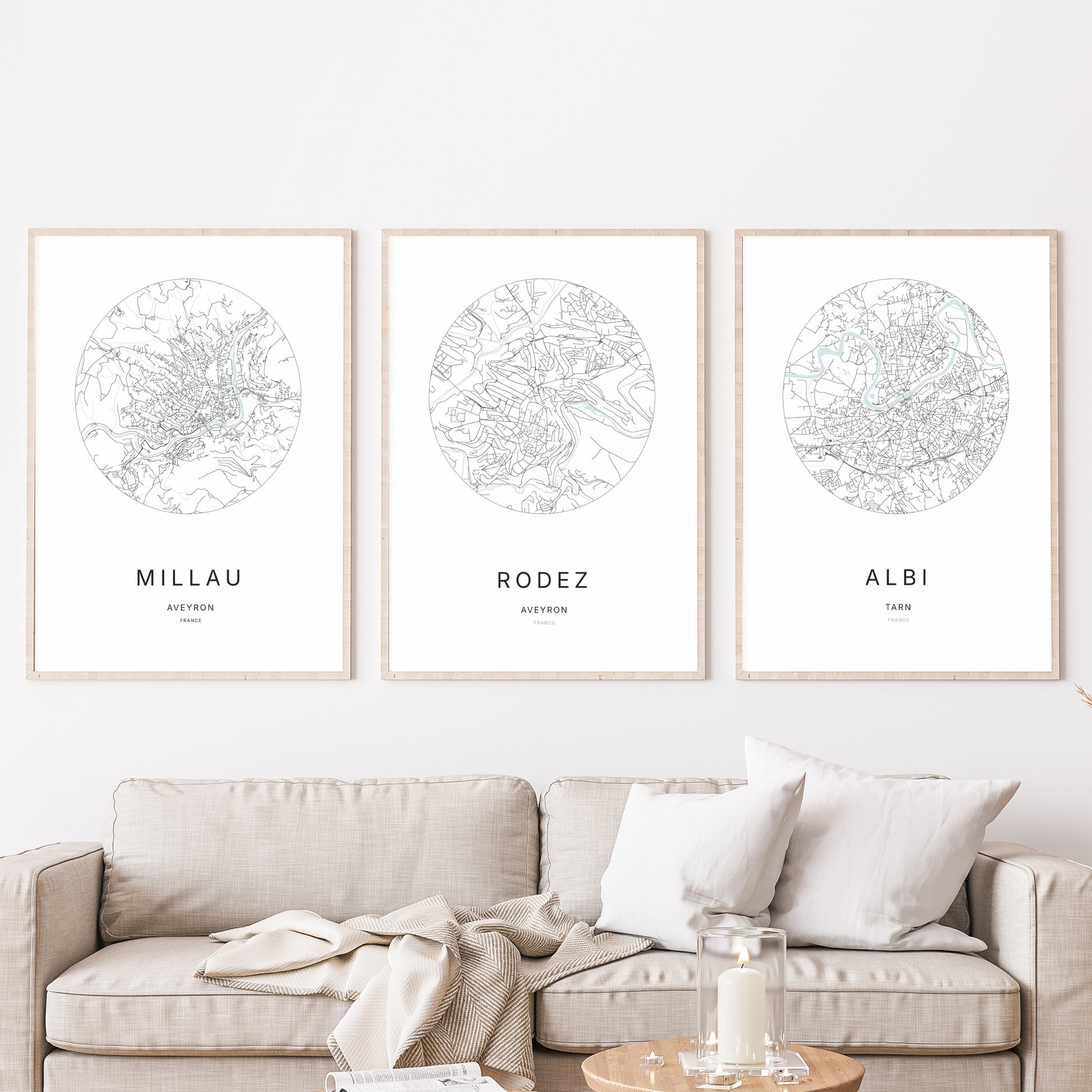 Composition murale de trois affiches minimalistes de villes (Rodez, Millau, Albi) encadrées au-dessus d’un canapé dans un salon moderne.