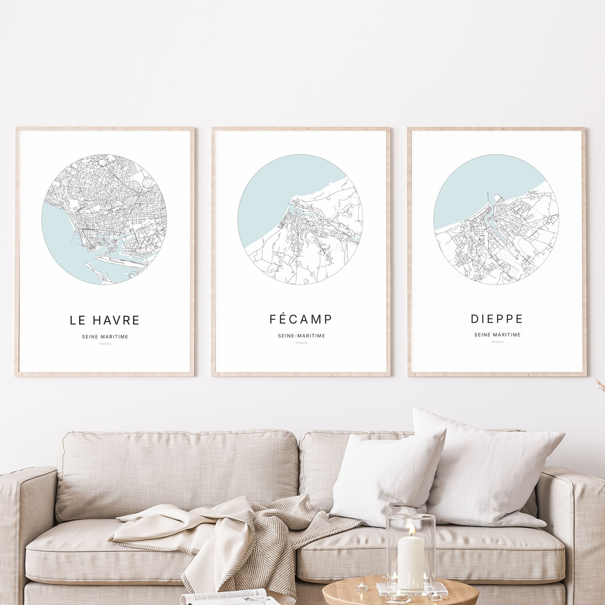 Composition murale de trois affiches minimalistes de villes (Fécamp, Le Havre, Dieppe) encadrées au-dessus d’un canapé dans un salon moderne.