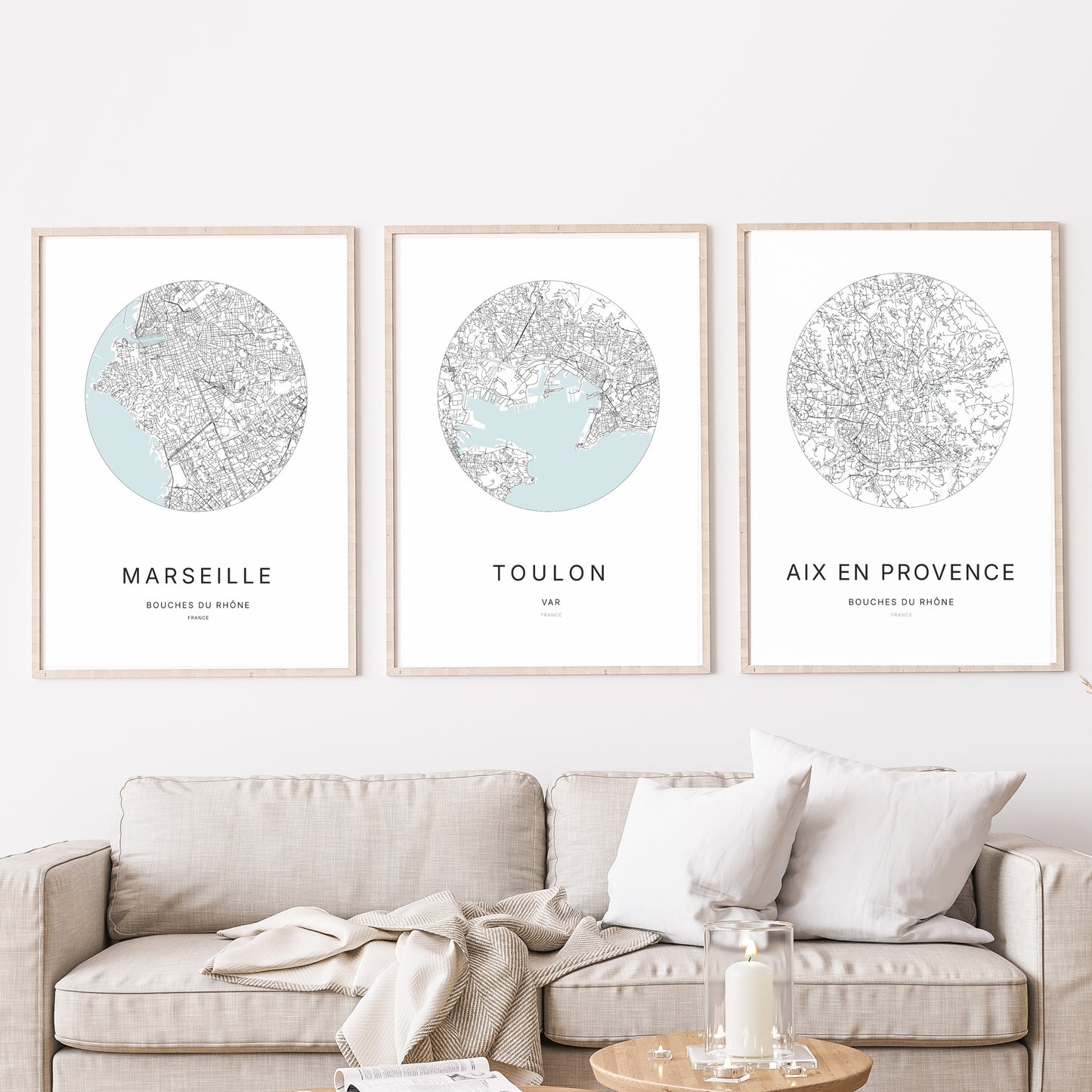 Composition murale de trois affiches minimalistes de villes (Marseille, Toulon, Aix-en-Provence) encadrées au-dessus d’un canapé dans un salon moderne